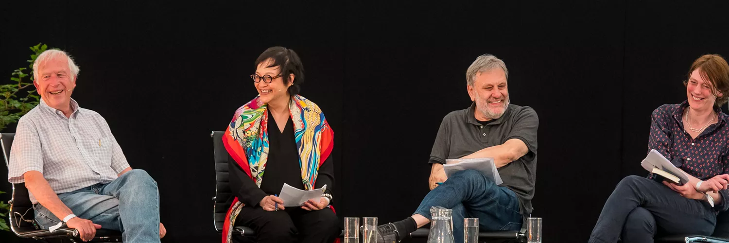 A group of four panelists seated on stage, engaged in discussion, with one woman wearing a colorful scarf and three men in casual attire.
