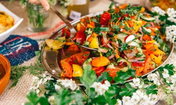 A vibrant platter of mixed colorful salad featuring tomatoes, peppers, and herbs, surrounded by fresh flowers and decorative table items.