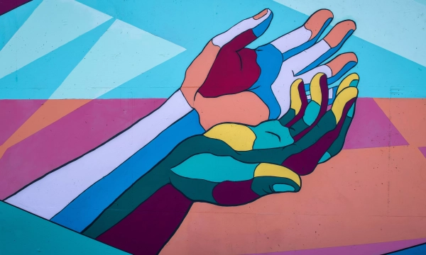A vibrant mural featuring stylized hands in various colors against a geometric background, symbolizing unity and connection.