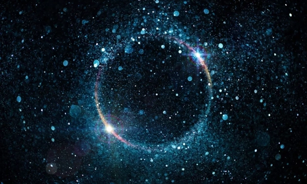 A cosmic scene featuring a circular formation of glowing particles and stars, set against a deep black background, resembling a galaxy or nebula.