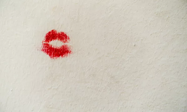 A red lipstick kiss mark on a textured white wall.
