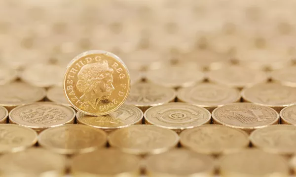 A close-up of various gold coins arranged in a flat pattern, with one coin prominently leaning against others, featuring a profile of Queen Elizabeth II.