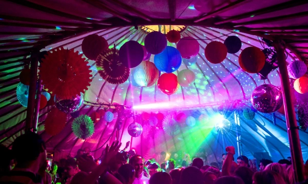 A vibrant party scene inside a tent, filled with colorful decorations and lights, as people dance under sparkling disco balls.
