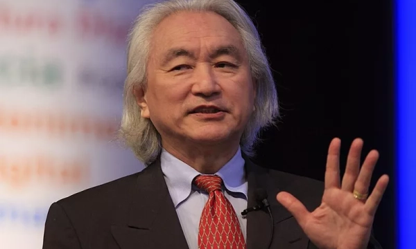 A man with long gray hair speaks at a podium, wearing a dark suit and red tie, gesturing with his right hand.