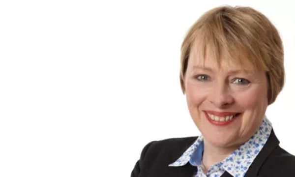 A smiling woman with short hair wearing a black blazer over a floral shirt, set against a white background.