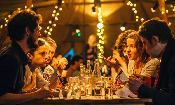 A diverse group of people engaged in an animated dinner conversation, surrounded by warm lighting and a cozy atmosphere inside a large tent.