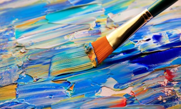 Close-up of a paintbrush applying vibrant blue and turquoise paint on a textured canvas, showcasing thick brush strokes and a mix of colors.