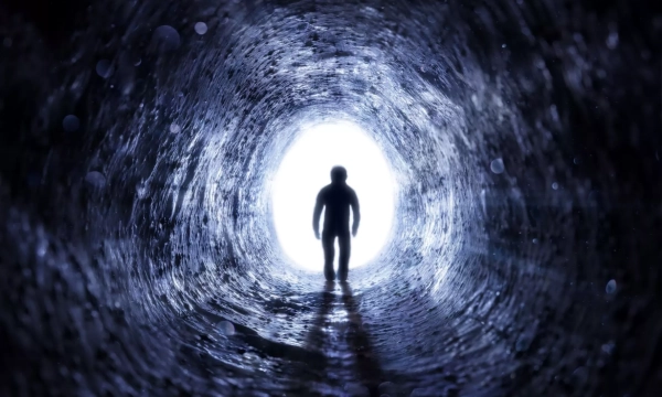 A silhouette of a figure stands at the end of a dark tunnel, illuminated by a bright light, creating a sense of mystery and depth.