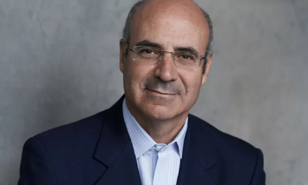 A middle-aged man with glasses and short hair, wearing a navy blazer over a light blue shirt, poses for a photograph against a neutral background.