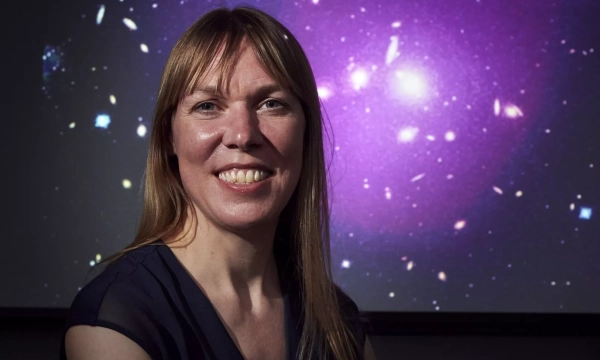 A woman with long, straight hair smiles in front of a colorful cosmic background filled with stars and galaxies.