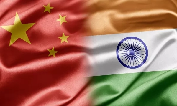 Flags of China and India juxtaposed, showcasing China's red flag with a yellow star and India's tricolor flag with saffron, white, and green sections featuring a navy blue wheel.