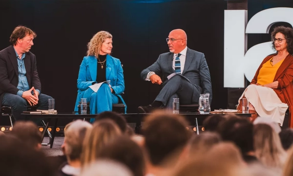 A panel discussion featuring four speakers, seated with microphones, discussing a topic in front of an audience.