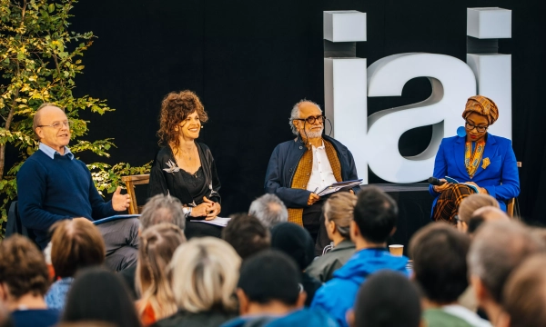 A panel discussion featuring four speakers in front of an audience, with the letters 