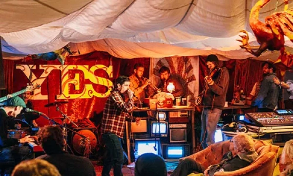 A lively underground music performance in a colorful, decorated room, featuring musicians playing instruments and an engaged audience enjoying the intimate setting.