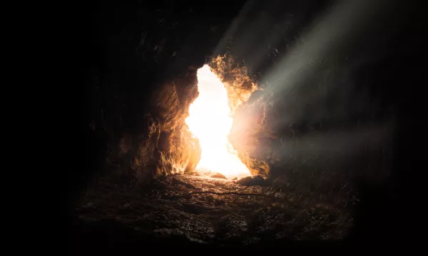 Light streams through the opening of a dark cave, illuminating the rocky interior and creating a mystical atmosphere.