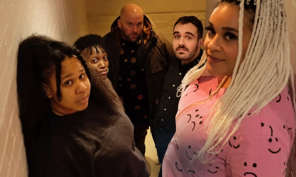 A diverse group of five individuals posing closely in a narrow stairwell, with various expressions and styles, highlighting a casual yet intimate atmosphere.