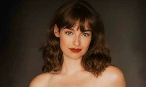 A woman with wavy brown hair and red lipstick is looking directly at the camera against a dark background.