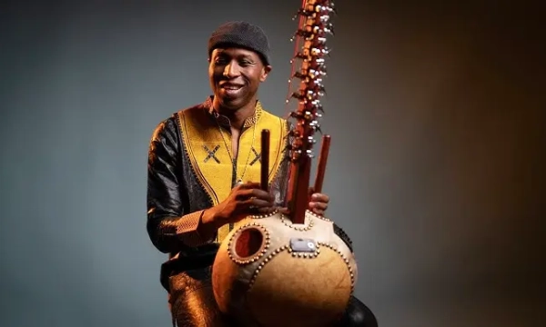 A musician playing a kora, a traditional West African string instrument, dressed in colorful attire with a warm smile, set against a dramatic background.