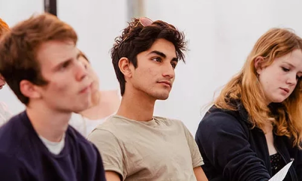Three young people attentively listen in a classroom setting, with a focus on the thoughtful expression of a young man in the center.