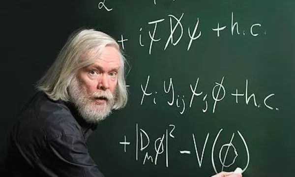 A bespectacled man with long gray hair writes equations on a chalkboard, showcasing complex mathematical formulas in a classroom setting.