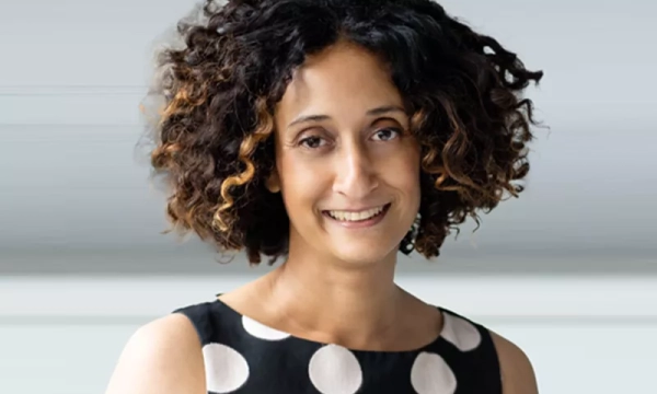 A woman with curly hair and a polka dot dress smiles warmly at the camera, set against a soft background.
