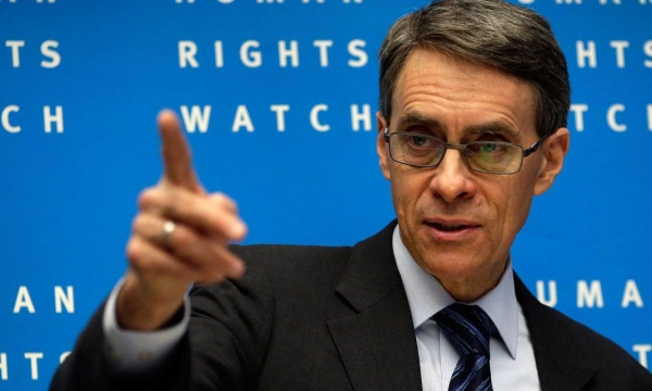A man with glasses in a suit gestures while speaking at a Human Rights Watch event, with blue background text reading "HUMAN RIGHTS WATCH."