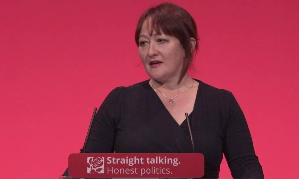 A woman speaking at a podium with a red backdrop, promoting themes of honesty and straightforwardness in politics.