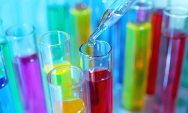 A close-up of a dropper adding a liquid to a red test tube, surrounded by colorful test tubes filled with various liquids in vibrant hues.