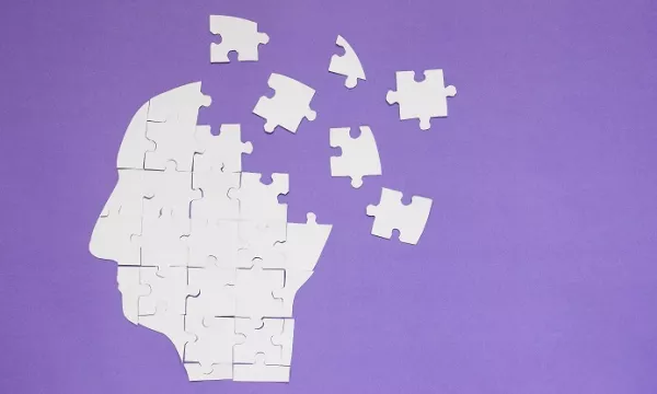 A silhouette of a head made from white puzzle pieces, with some pieces floating away against a purple background, symbolizing the concept of missing pieces in understanding the mind.