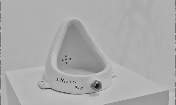 A white urinal sculpture displayed on a pedestal, inscribed with "R. Mutt 1917," referencing Marcel Duchamp's famous artwork.