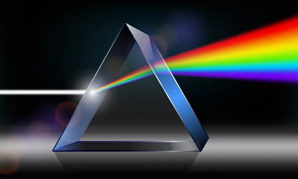 A triangular glass prism dispersing white light into a rainbow spectrum. The background is dark, enhancing the vibrant colors of the light.