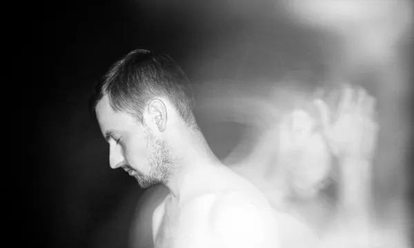 A man with short hair and a light beard is shown in profile, appearing contemplative against a soft, blurred background.