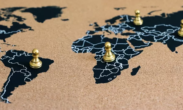 A world map on cork with golden game pieces strategically placed across different continents, highlighting various geographic regions.