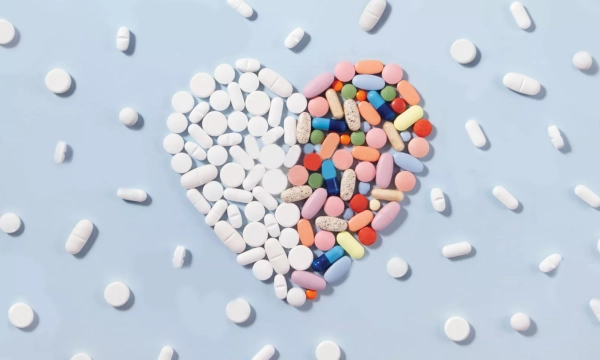 A heart shape made of various pills and tablets, surrounded by scattered white capsules and colorful medication, symbolizing health and wellness.