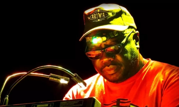 A musician wearing a cap and glasses is focused on playing a keyboard, illuminated by stage lights.