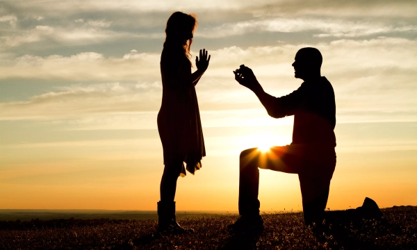 A silhouette of a man proposing to a woman against a sunset backdrop, capturing a romantic moment in an outdoor setting.