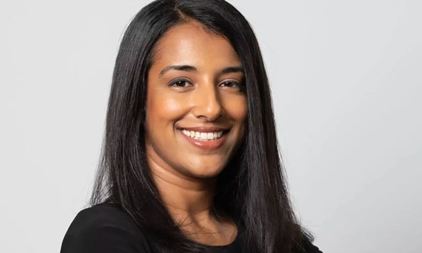 A smiling woman with long black hair and a black top poses confidently against a light gray background.