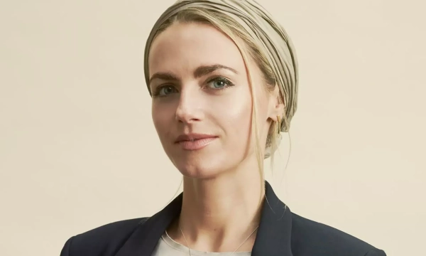 Portrait of a woman with a headscarf, wearing a blazer, against a light background, exuding confidence and professionalism.