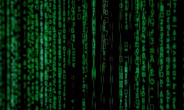 A close-up of green digital code cascading down a dark background, reminiscent of a matrix-style visual effect.