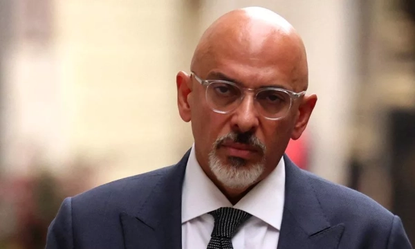 A bald man in a dark suit and glasses walking down a street, with a serious expression on his face.
