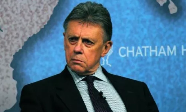 A man in a suit looking seriously at the camera, seated against a blue backdrop with "Chatham House" visible.
