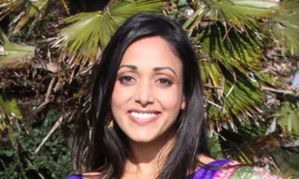 A woman smiling in traditional attire stands in front of a palm tree, showcasing a vibrant cultural outfit against a natural backdrop.