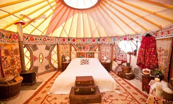 Interior of a beautifully decorated yurt, featuring vibrant textiles, a central bed, traditional storage chests, and ornate patterns on walls and ceiling.