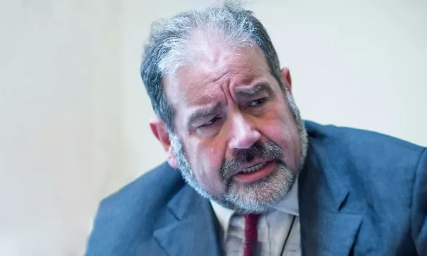 A man with a beard and suit appears to be engaged in an intense discussion, showing a serious expression.