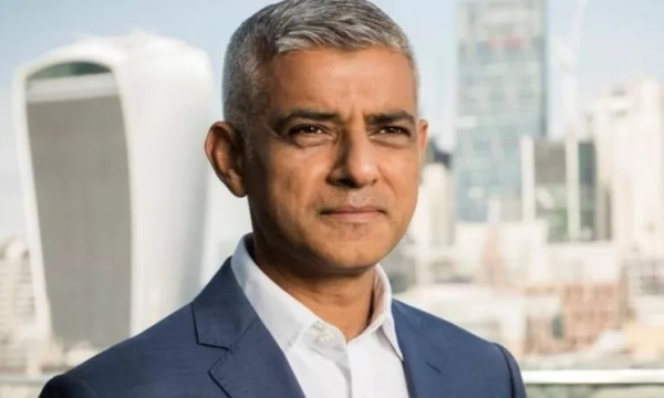 A man with short gray hair, wearing a navy suit and white shirt, stands confidently against a modern city skyline.