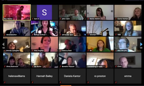 A Zoom video call featuring multiple participants in a grid format, including a speaker in the top left corner, with varying expressions and gestures among the attendees.