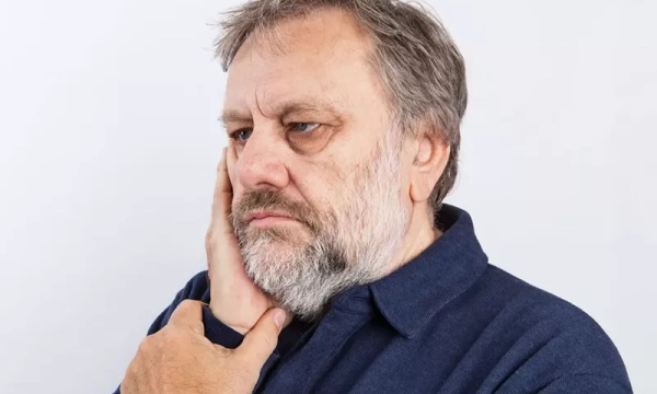 A pensive middle-aged man with a beard, wearing a navy blue shirt, appears deep in thought against a plain white background.