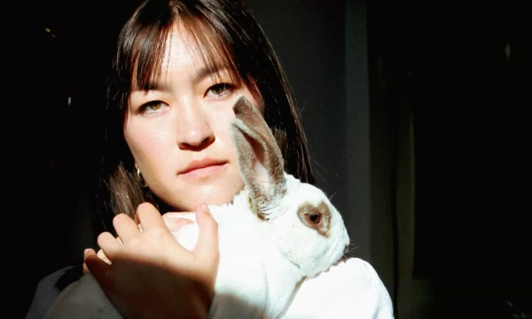 A young woman with dark hair holds a white rabbit closely, illuminated by soft natural light. The image conveys warmth and intimacy.