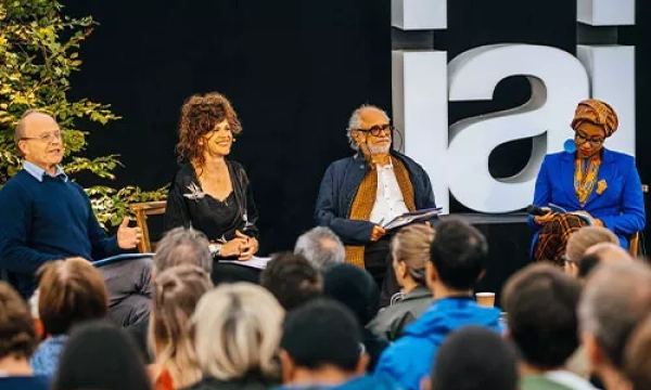 A panel discussion featuring four speakers seated on stage, with an audience in front, and the letters "iai" prominently displayed in the background.