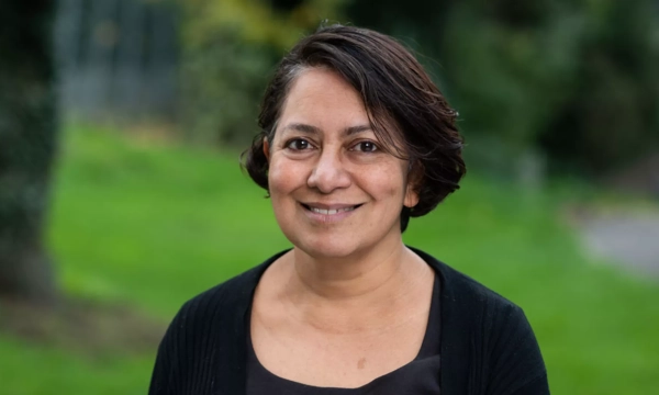 Portrait of a smiling woman with short, dark hair, wearing a black cardigan, against a blurred green background.